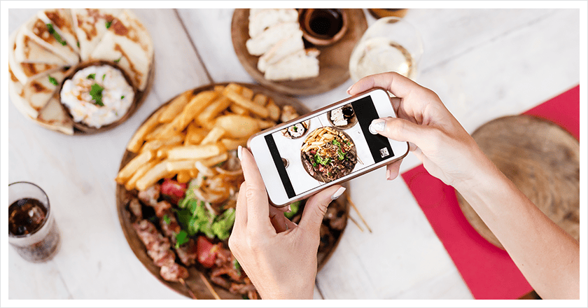 Osoba trzyma smartfona nad talerzami z jedzeniem w celu zrobienia zdjęcia